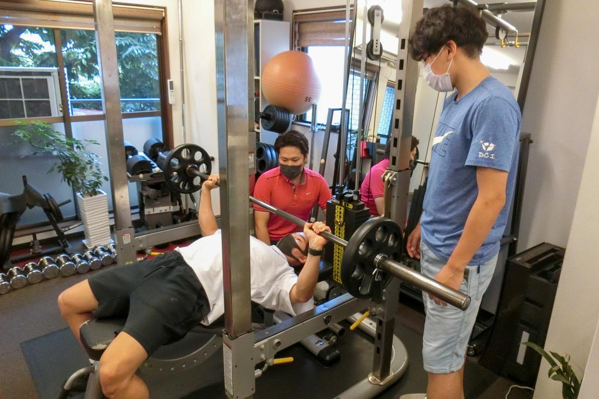 ベンチプレスをする金原さんと指導する新藤さん（左）、補助する武内さん