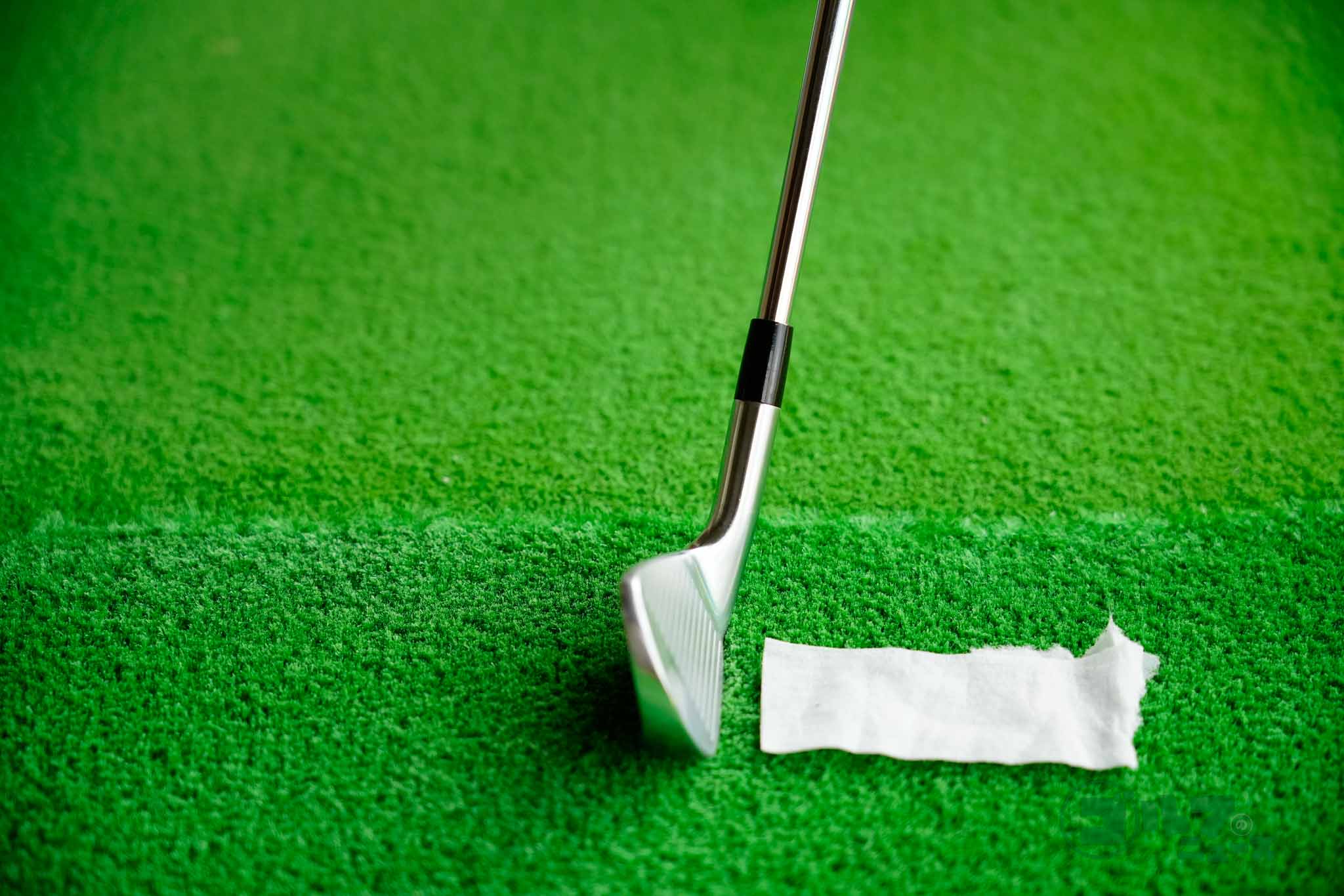 ボールの1個分先にガムテープや絆創膏をマットの上に貼る。それをはがすつもりでヘッドを下ろしてくると、自然とダウンブローの軌道になる。アッパーブローだとはがすことができないので注意　写真:鈴木祥